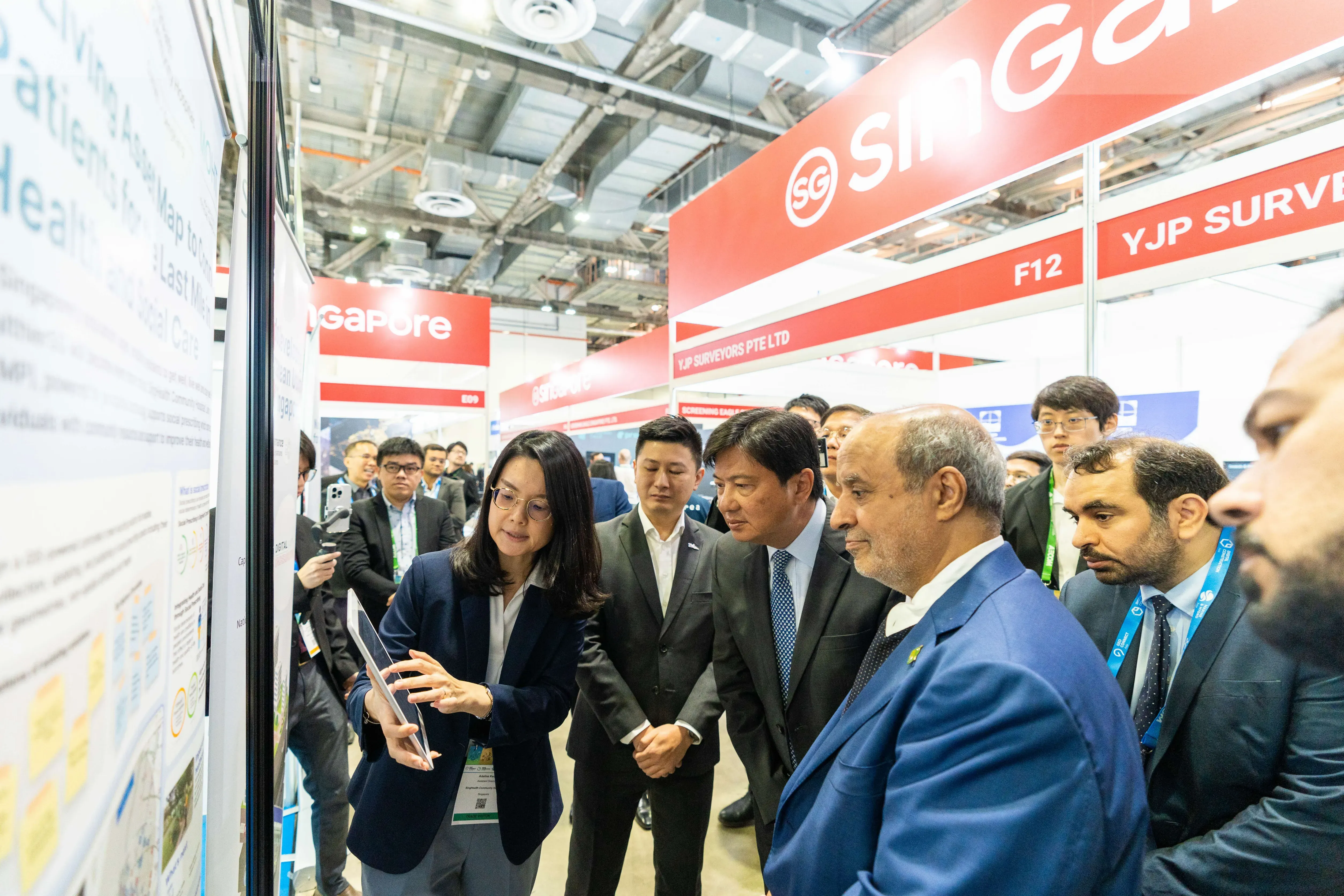 A woman presents a tablet to a group of suited attendees at a Singapore trade exhibition hall.